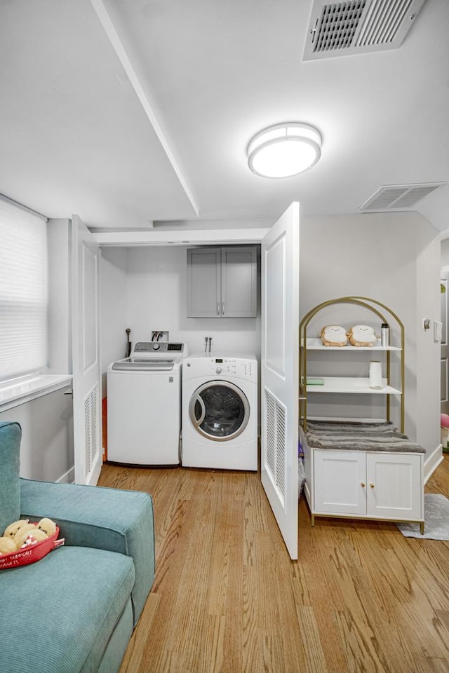 laundry room featuring light wood-type flooring, visible vents, cabinet space, and washer and clothes dryer