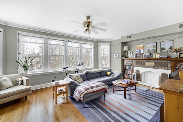 living area featuring a fireplace, wood finished floors, visible vents, and crown molding