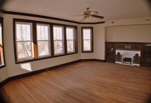 unfurnished living room featuring baseboards, a fireplace, ornamental molding, and wood finished floors