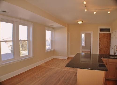 kitchen with baseboards, dark countertops, a peninsula, light wood-type flooring, and a sink