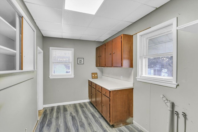 kitchen with brown cabinetry, light countertops, a drop ceiling, and wood finished floors