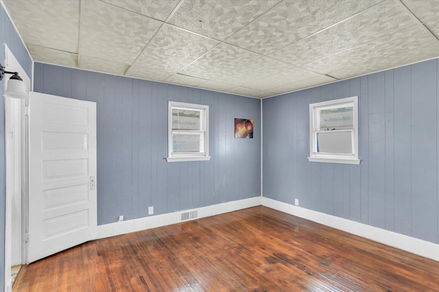 empty room featuring visible vents, hardwood / wood-style flooring, and baseboards