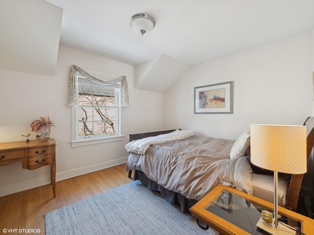 bedroom with vaulted ceiling, wood finished floors, and baseboards