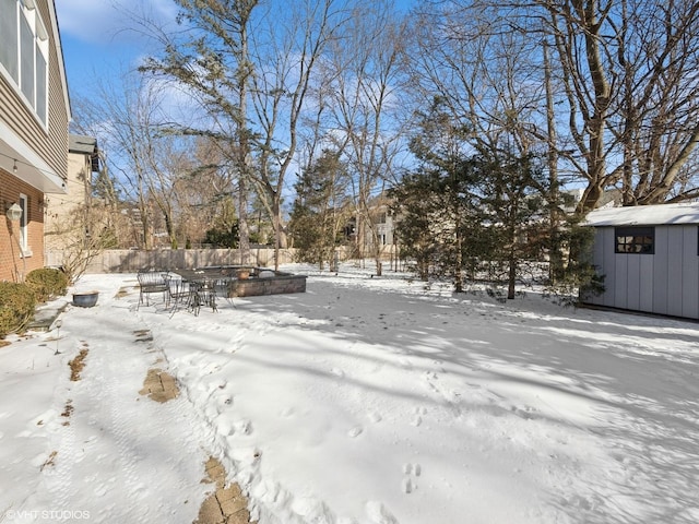 yard covered in snow with outdoor dining space, a storage unit, an outdoor structure, and fence