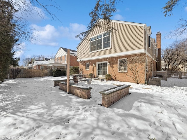 snow covered rear of property featuring a patio, brick siding, and fence