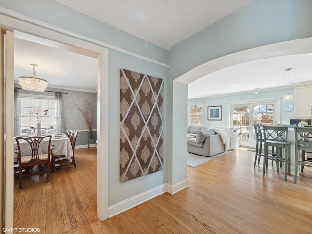 hall featuring light wood-type flooring, baseboards, arched walkways, and a healthy amount of sunlight