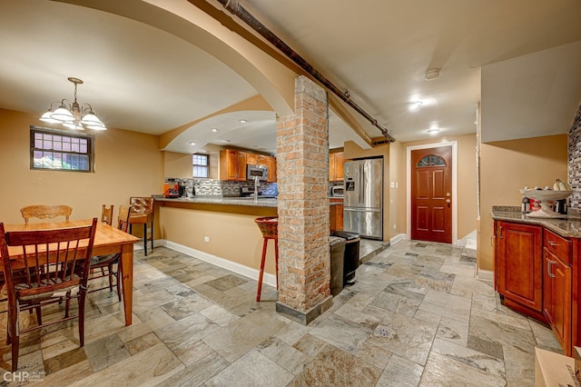 kitchen with a notable chandelier, stone tile floors, stainless steel appliances, tasteful backsplash, and baseboards