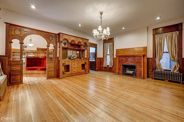 living room featuring light wood-type flooring, wainscoting, a fireplace, and radiator heating unit