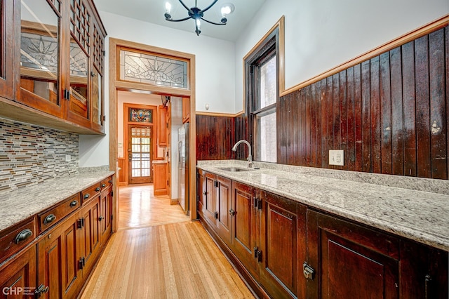 interior space featuring tasteful backsplash, stainless steel fridge, a wainscoted wall, light wood-style flooring, and a sink