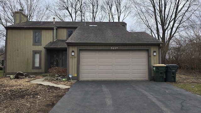 view of front of home with a shingled roof, driveway, a chimney, and an attached garage