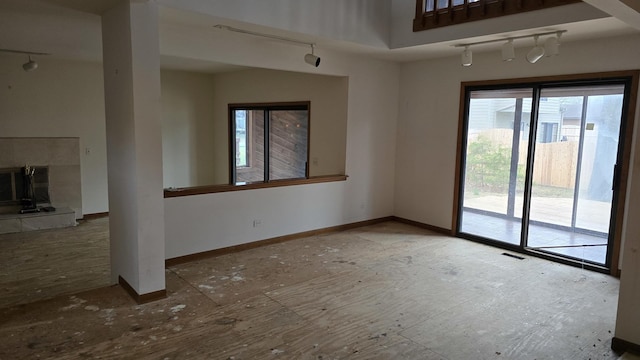 empty room with visible vents, a tiled fireplace, baseboards, and track lighting