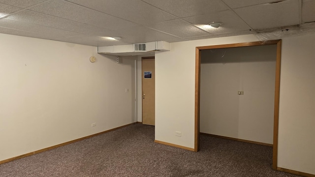 finished below grade area with a paneled ceiling, baseboards, visible vents, and dark carpet