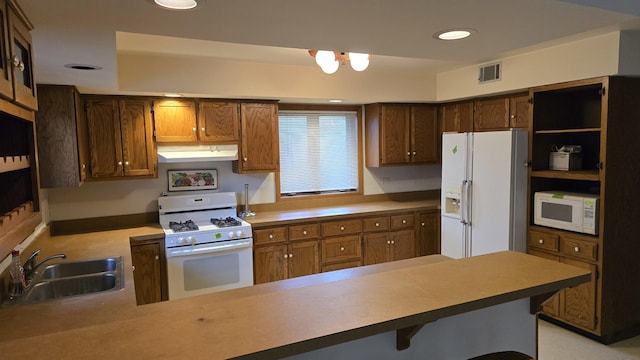 kitchen with a breakfast bar area, visible vents, a sink, white appliances, and a peninsula