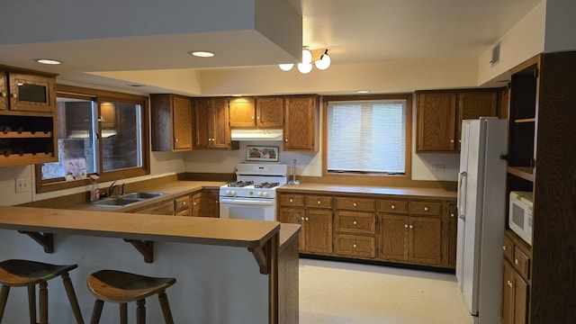 kitchen with white appliances, brown cabinets, a peninsula, a kitchen bar, and a sink