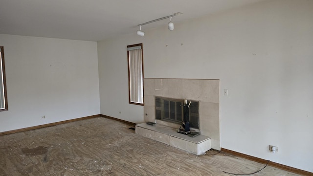 unfurnished living room featuring rail lighting, a fireplace, and baseboards