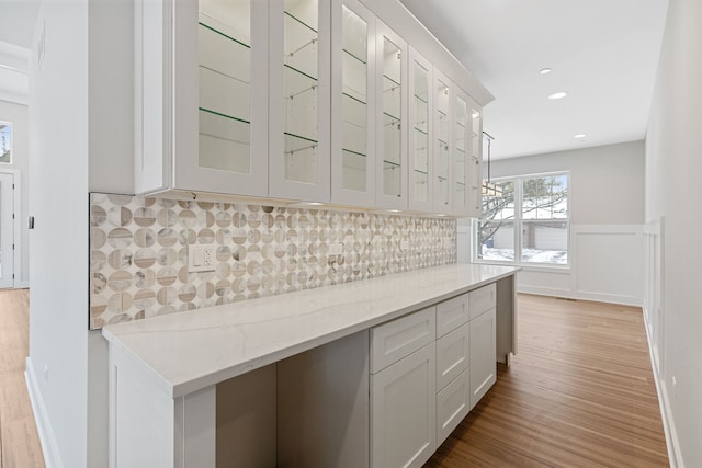 kitchen featuring light stone counters, wood finished floors, white cabinets, decorative backsplash, and glass insert cabinets