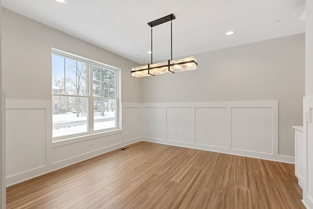 unfurnished dining area with light wood-style floors, a decorative wall, a notable chandelier, and recessed lighting