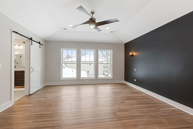 unfurnished room with a barn door, wood finished floors, visible vents, baseboards, and a ceiling fan