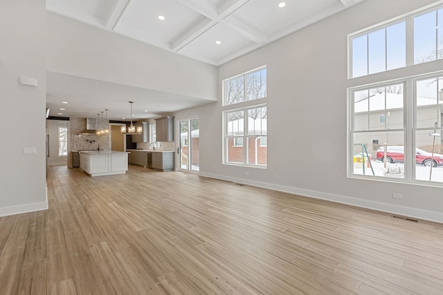 unfurnished living room featuring baseboards, visible vents, light wood-style flooring, and a notable chandelier