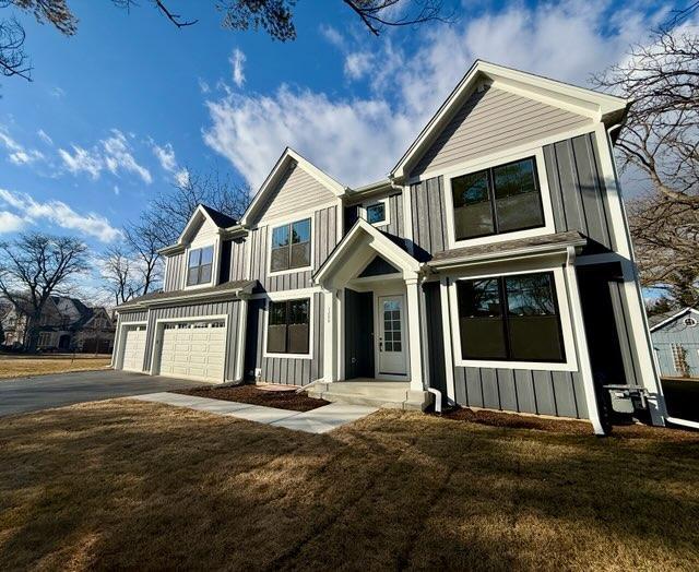 view of front facade with board and batten siding, a front yard, an attached garage, and aphalt driveway