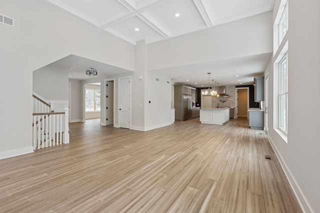 unfurnished living room with stairway, light wood-style flooring, a high ceiling, coffered ceiling, and baseboards