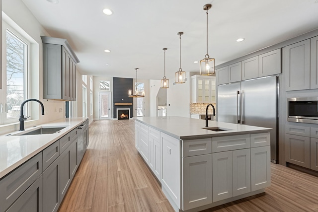 kitchen with gray cabinets, a sink, an island with sink, and built in appliances