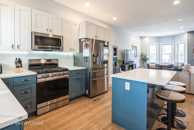 kitchen with light wood finished floors, stainless steel appliances, decorative backsplash, open floor plan, and white cabinets