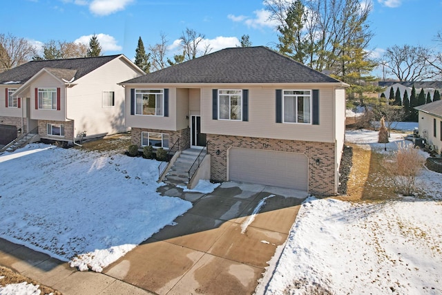 raised ranch featuring concrete driveway, brick siding, an attached garage, and a shingled roof