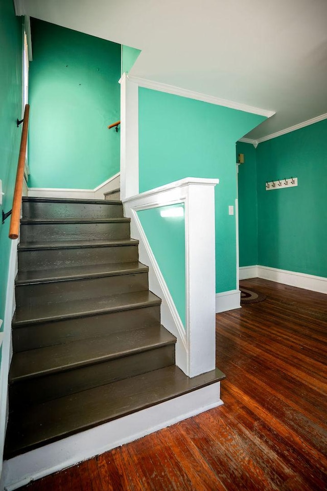 stairway with baseboards, wood finished floors, and crown molding