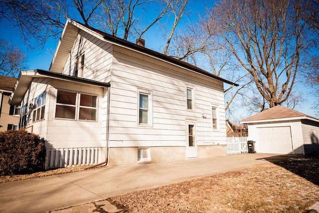 view of side of home with an outdoor structure, fence, a detached garage, concrete driveway, and a chimney