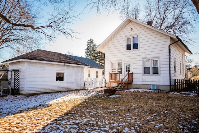 snow covered house featuring fence and a chimney