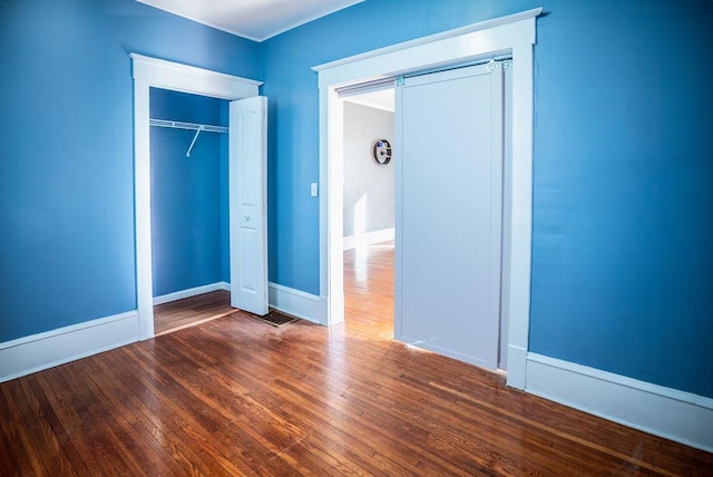 unfurnished bedroom featuring dark wood-type flooring, a closet, baseboards, and a barn door