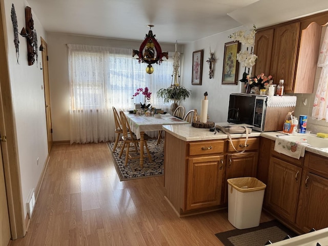 kitchen featuring brown cabinets, light wood finished floors, stainless steel microwave, and light countertops