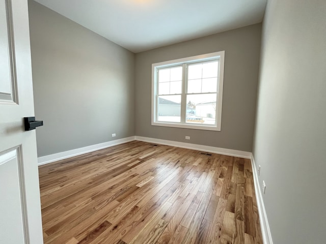 empty room with light wood-type flooring, visible vents, and baseboards