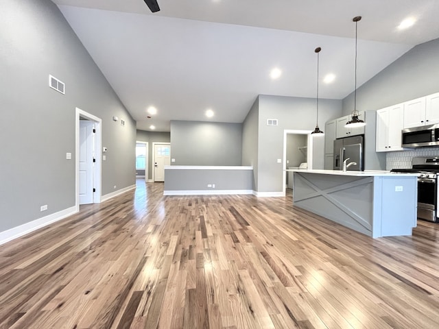 kitchen featuring an island with sink, decorative light fixtures, stainless steel appliances, light countertops, and white cabinetry