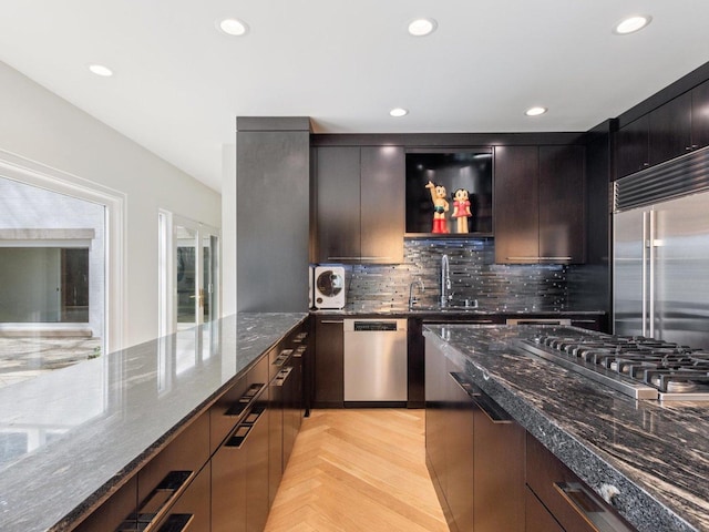 kitchen with a sink, stainless steel appliances, tasteful backsplash, and dark stone counters