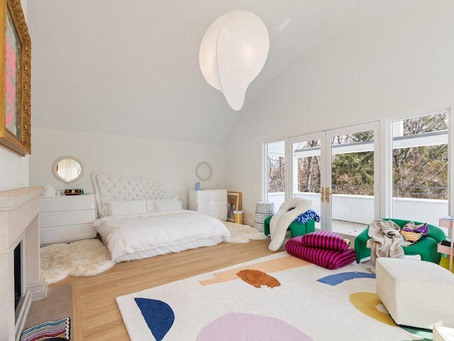 bedroom with a fireplace with raised hearth, french doors, high vaulted ceiling, and wood finished floors