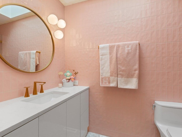 bathroom with vanity, tile walls, a skylight, and toilet