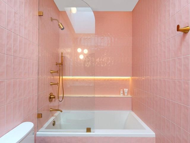 bathroom featuring tiled shower / bath combo, toilet, and tile walls