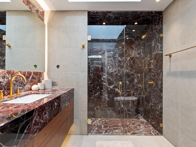 full bathroom with a marble finish shower, tile walls, and vanity