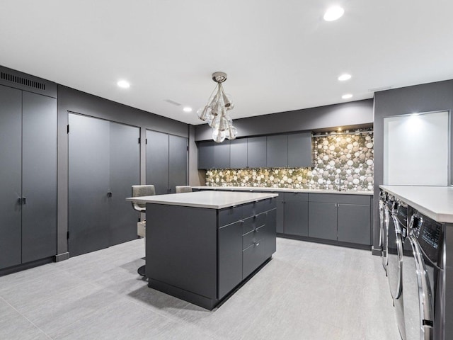 kitchen with gray cabinets, decorative light fixtures, backsplash, a kitchen island, and light countertops