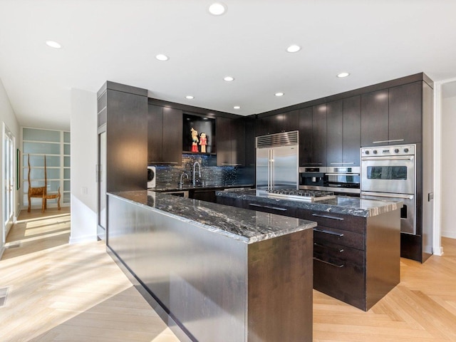 kitchen with dark stone counters, a sink, appliances with stainless steel finishes, tasteful backsplash, and a center island