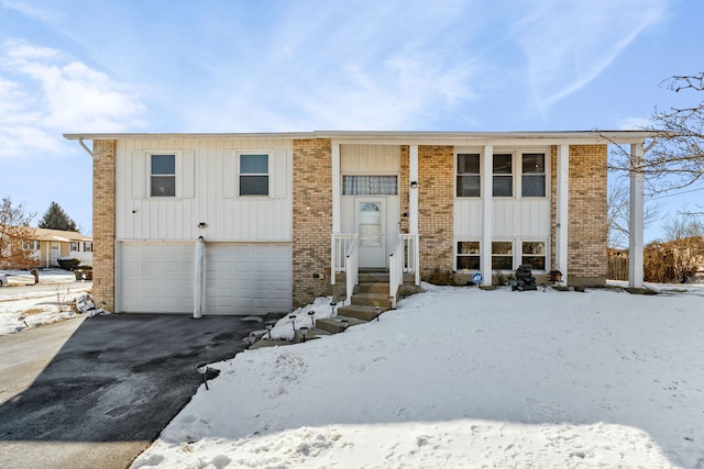 split foyer home with board and batten siding, aphalt driveway, an attached garage, and brick siding