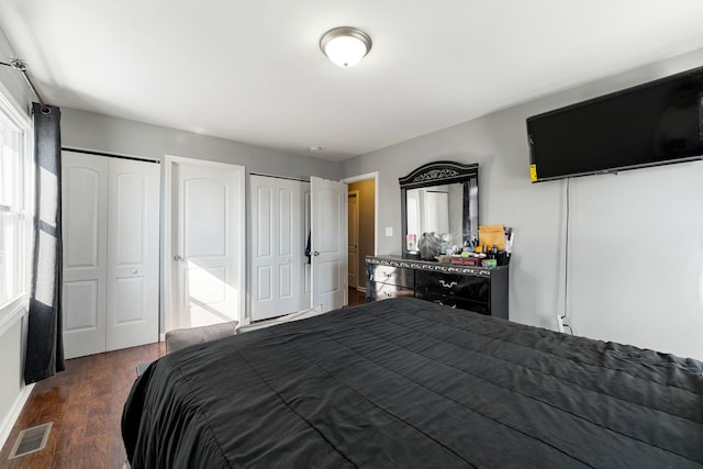 bedroom featuring dark wood-style floors, visible vents, and two closets