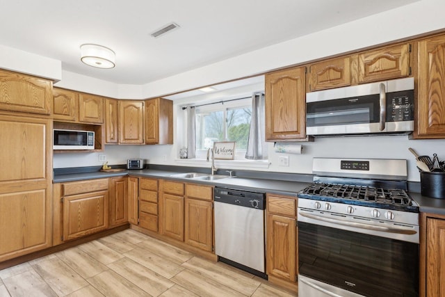 kitchen with light wood-style floors, dark countertops, a sink, stainless steel appliances, and brown cabinets