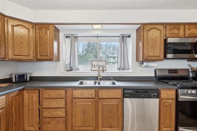 kitchen with a sink, appliances with stainless steel finishes, dark countertops, and brown cabinets