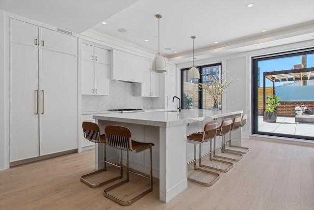 kitchen featuring a breakfast bar, decorative light fixtures, light countertops, white cabinetry, and an island with sink