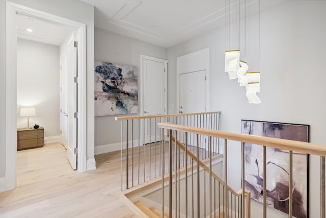 hall featuring attic access, baseboards, light wood finished floors, and an upstairs landing