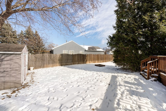 yard covered in snow featuring an outbuilding, a fenced backyard, and a storage unit