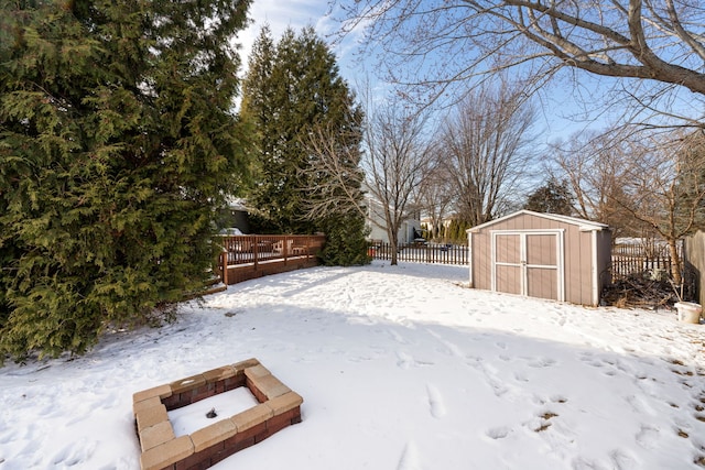 yard layered in snow with fence, a fire pit, an outdoor structure, and a shed